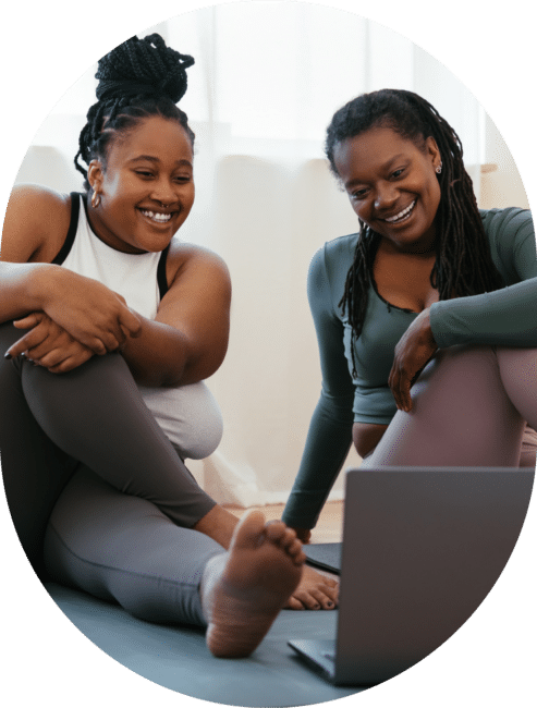 Two women sitting on a yoga mat together working with an online health coach